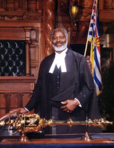 man in legislation robes standing behind desk , speakers mace on desk