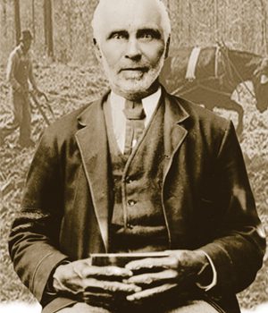 senior man seated facing camera holding what is likely a bible with two hands at his lap
