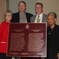 MWG Plaque Presentation 4 people stand behind bronze plaque that is resting on a table