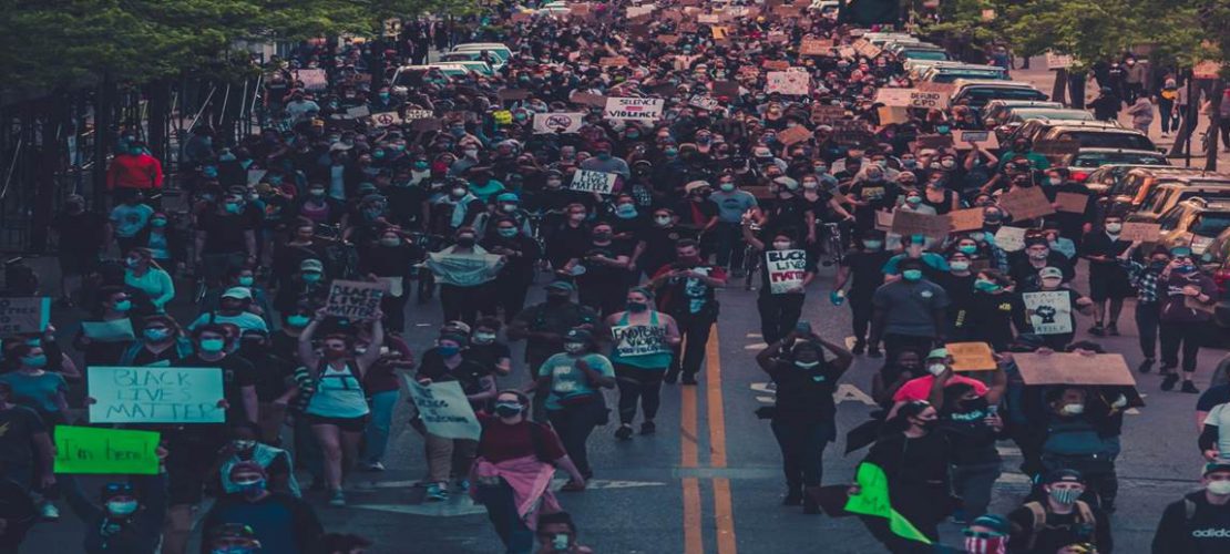 Wide tree-lined two lane street filled with people marching and holding signs