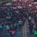 Wide tree-lined two lane street filled with people marching and holding signs