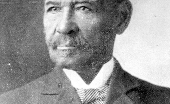 Portrait. Black male age 50, dressed semi-formally wearing jacket, vest, winged-collar white shirt with a striped pattern bow-tie