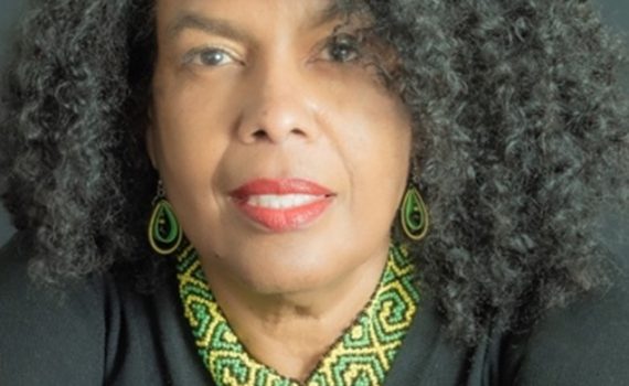 portrait black women with long curled hair smile wearing decorative earrings and necklace, black v-neck blouse