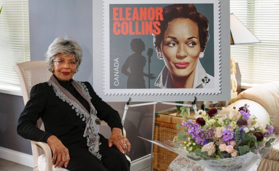 eleanor collins sitting with commemorative stamp poster on easel on the right