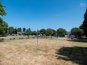 open grassy field tree lined playground homes are at the far end