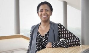 upper body of black woman, business attire, standing at counter-height table, right arm resting on table