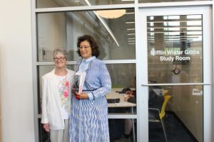 2 women standing close together background is glass panel wall and glass door to small room