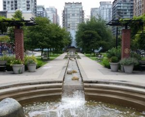 Park setting with concrete waterway running the length of the park, paved walkway, seating, greenspace on either side