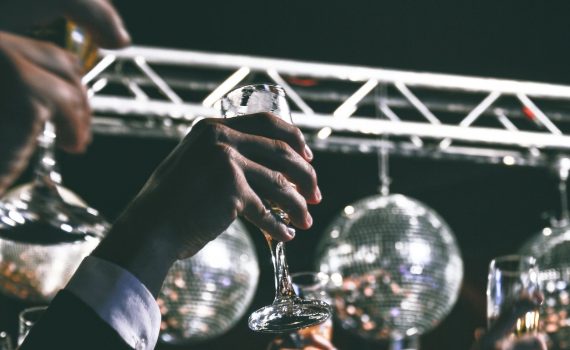camera angle is upward, gala setting with lighted suspended globes, upper torso of guests shown with glasses raised