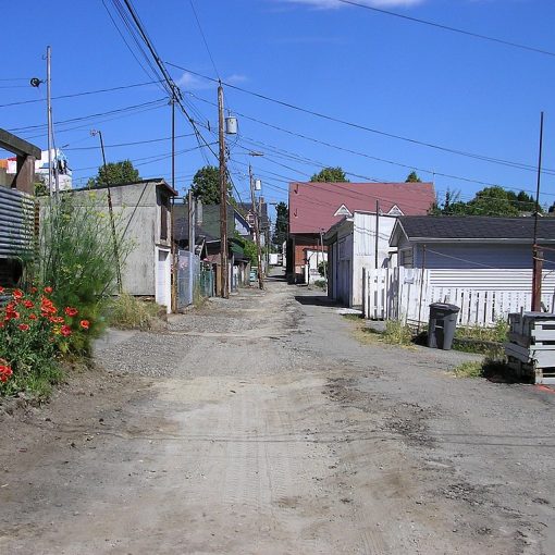 colour photo dirt road alley with housing, structures on either side