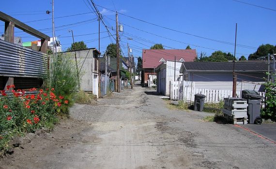 colour photo dirt road alley with housing, structures on either side