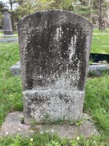 In cemetery, very stained, darkened tarnished marble column, inscription is mostly obscured