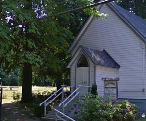white clapboard church with peak roof and signage at the front