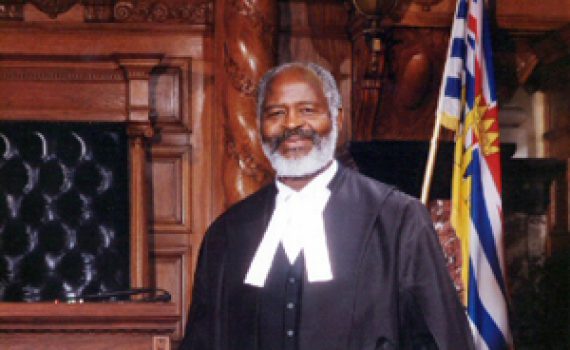 man in legislation robes standing behind desk , speakers mace on desk