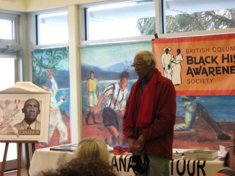 senior black man standing addresses the audience, poster of fergie jenkins stamp on easel at left