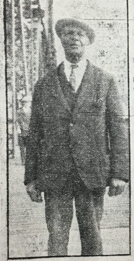 senior man standing with arms at side in suit and hat