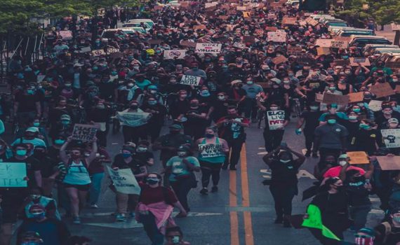 Wide tree-lined two lane street filled with people marching and holding signs