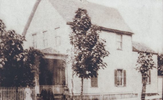 sepia toned taken from side angle of 2 story shingled and gabled house with porch, fence and trees at front house