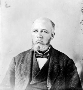 b&w portrait, older man, balding with salt & pepper short beard and sideburns, dressed in suit with vest, white shirt and bowtie