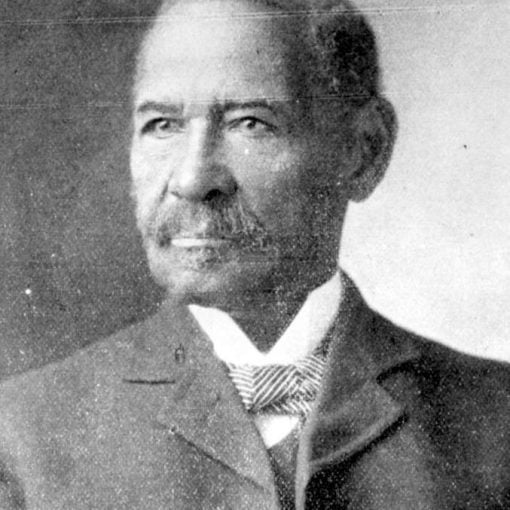 Portrait. Black male age 50, dressed semi-formally wearing jacket, vest, winged-collar white shirt with a striped pattern bow-tie