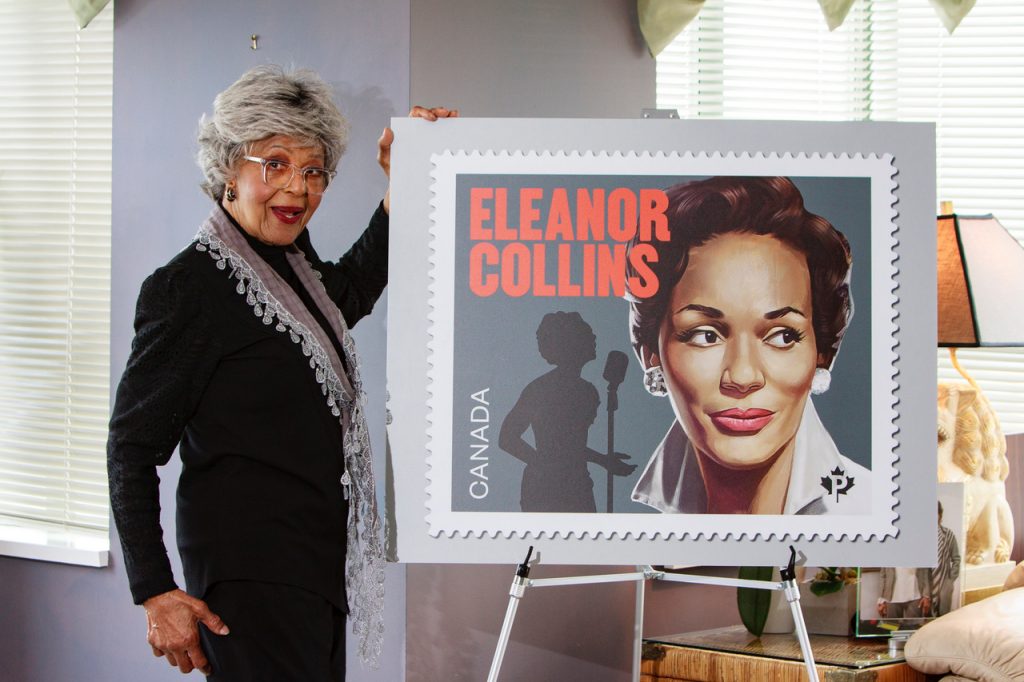 eleanor collins standing left hand on poster of commemorative stamp