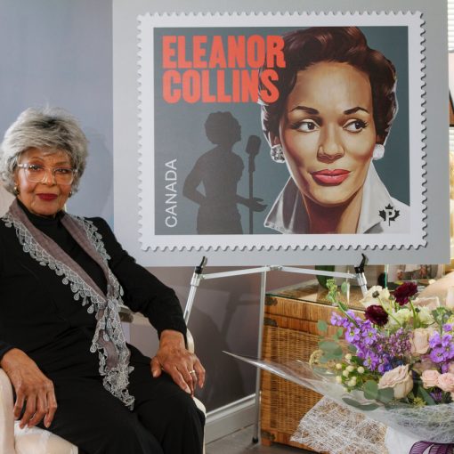 eleanor collins sitting with commemorative stamp poster on easel on the right