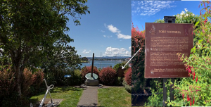 Small parklike space, shrubs at far end overlooking harbour, center, short paved walkway leads to Indigenous marker and bronze plaque