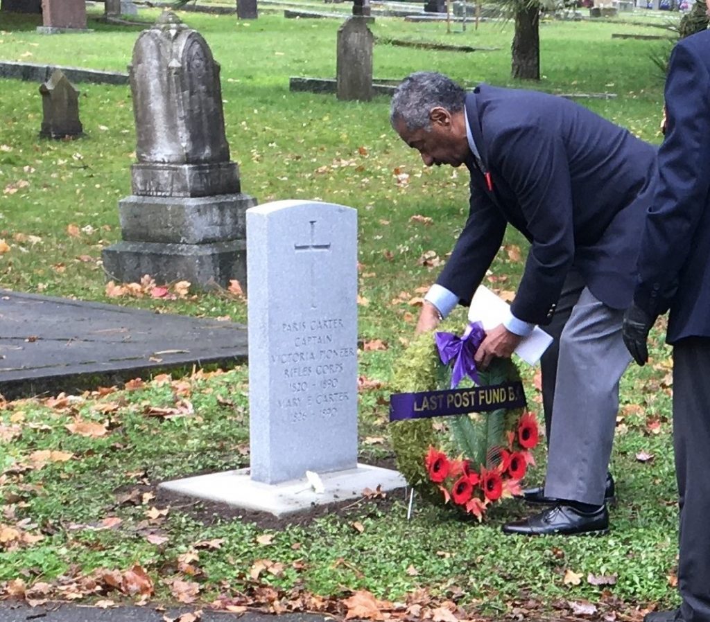 man in suit, stooping and placing wreath at grave marker