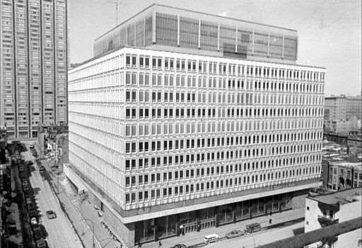 gray-toned image of 11 story concrete building with prominent windows in city-scape