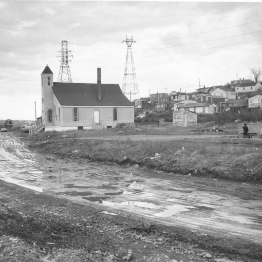 b&w side view of church prominent on right left side, dirt road, houses on slope on the right side (behind the church)