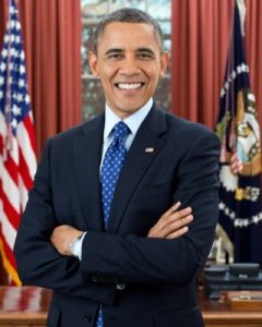 man in suit standing with arms folded and smiling in US president office, american flag and other regalia in background