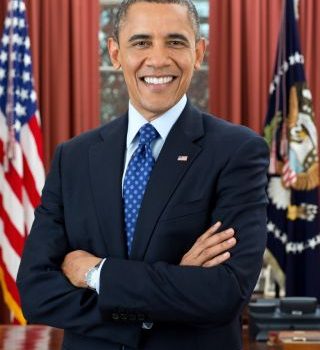 man in suit standing with arms folded and smiling in US president office, american flag and other regalia in background