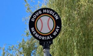 circle with black background, centre is white baseball with traditional African colors for border and stitching; bold white text in circle border