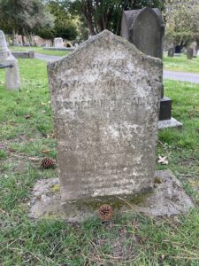 In cemetery, dark tarnished marble tablet with angled top on mossy concrete base