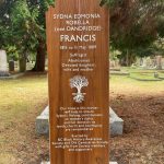 medium-colored wooden-stained grave marker with white lettering, carved tree outline in white is centred