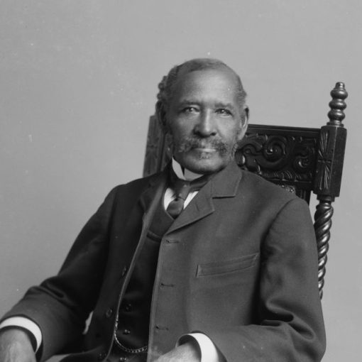 : photo b&w- man with pleasant smile, moustache looking directly at the camera - seated in a chair