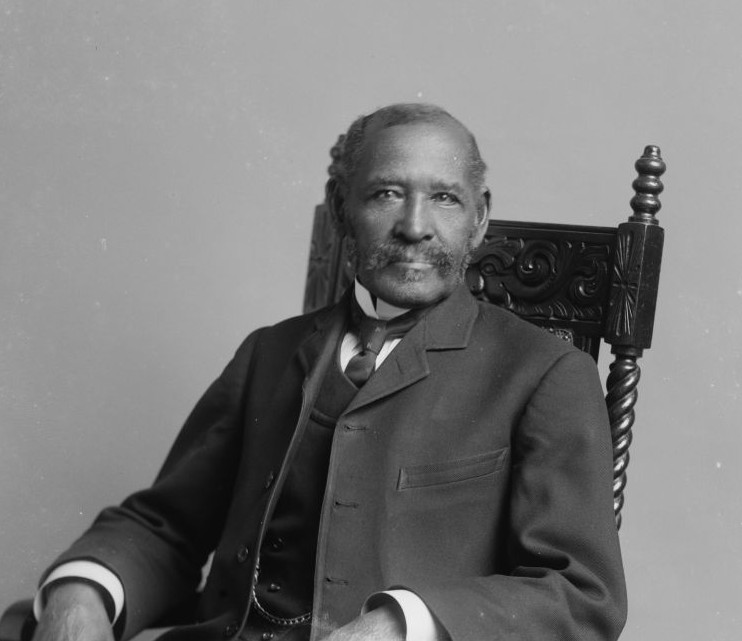 : photo b&w- man with pleasant smile, moustache looking directly at the camera - seated in a chair